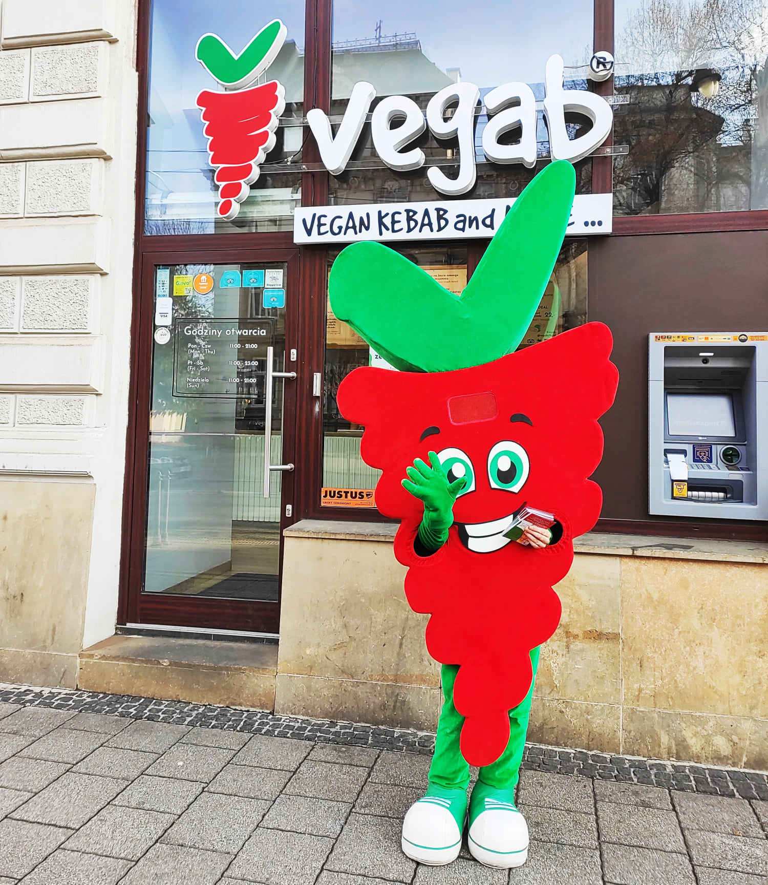 Na fotografii widnieje kostium reklamowy Marchewka Vegab pozujący do zdjęcia przed lokalem firmy Vegab